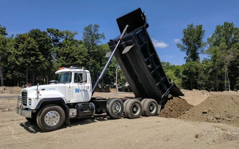 White dump truck unloading dirt at a construction site with its bed raised.