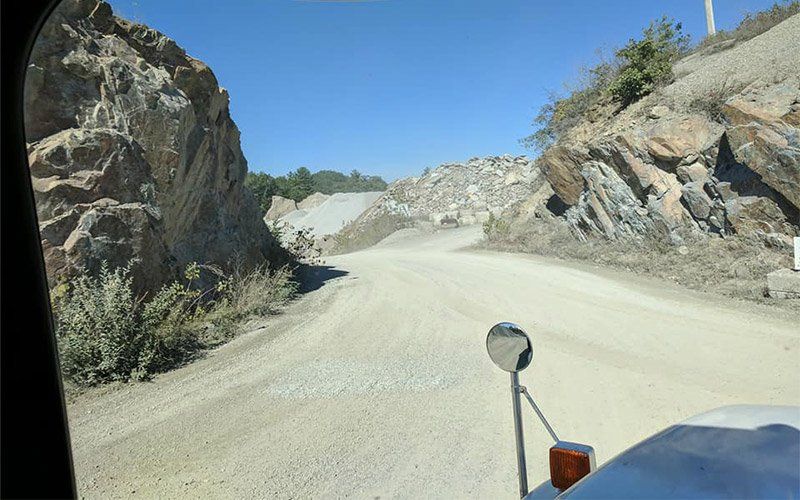 Dirt road winding through rocky hills under a clear blue sky, viewed from a vehicle