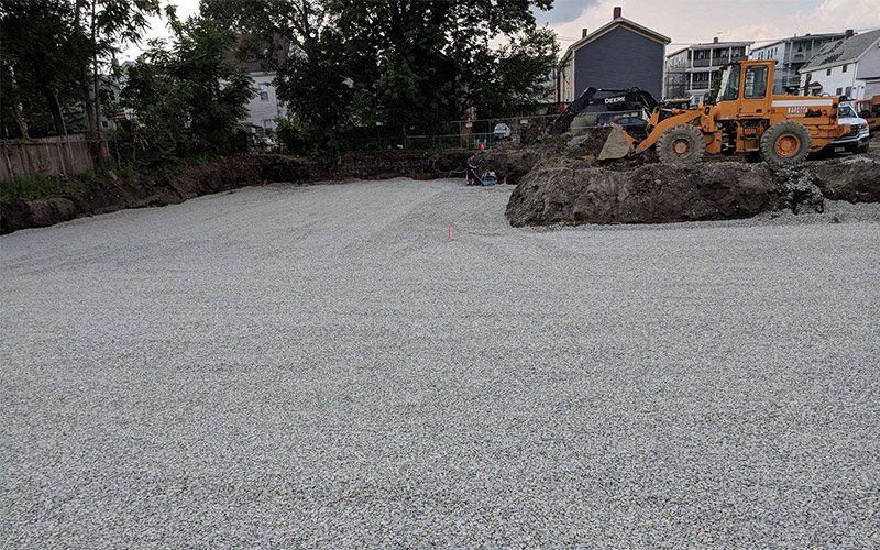 Construction site with a yellow loader moving gravel beside a dirt road at dusk