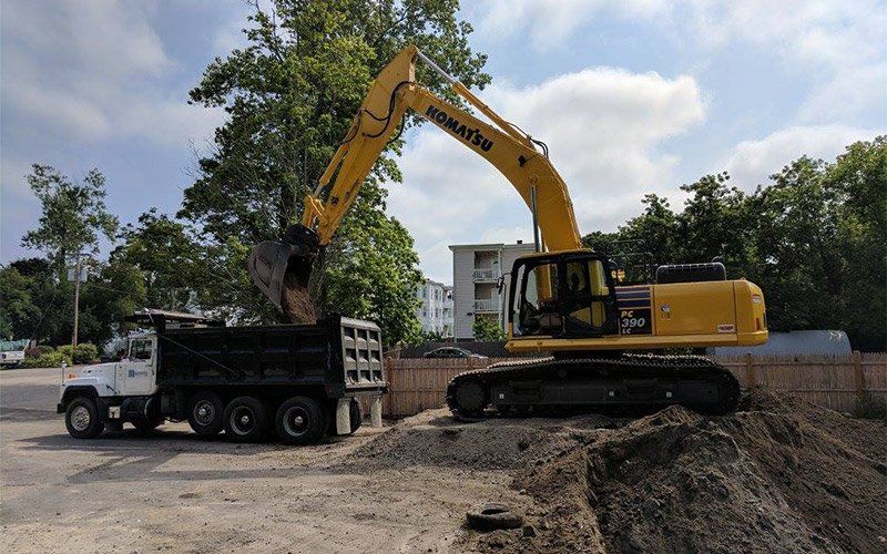 Yellow excavator loading dirt into a dump truck at a construction site.
