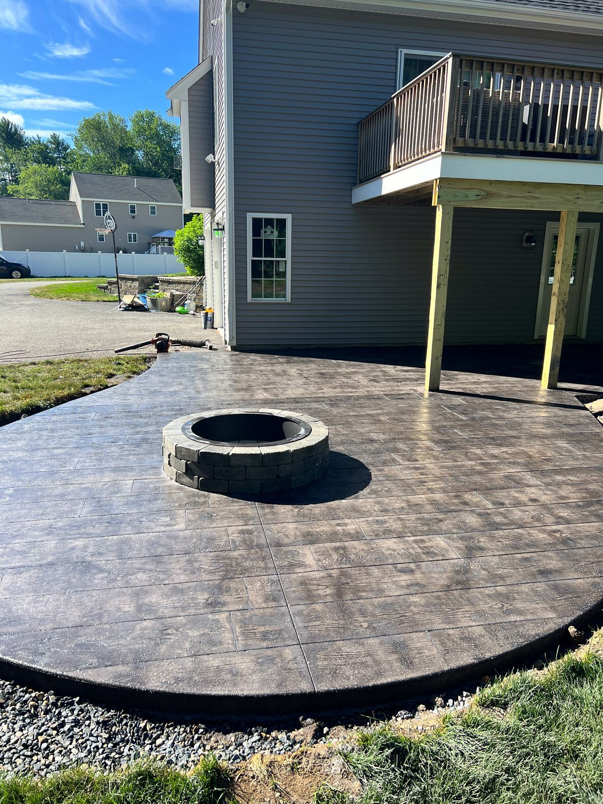 Backyard with stamped concrete patio, circular fire pit, and raised deck beside a house