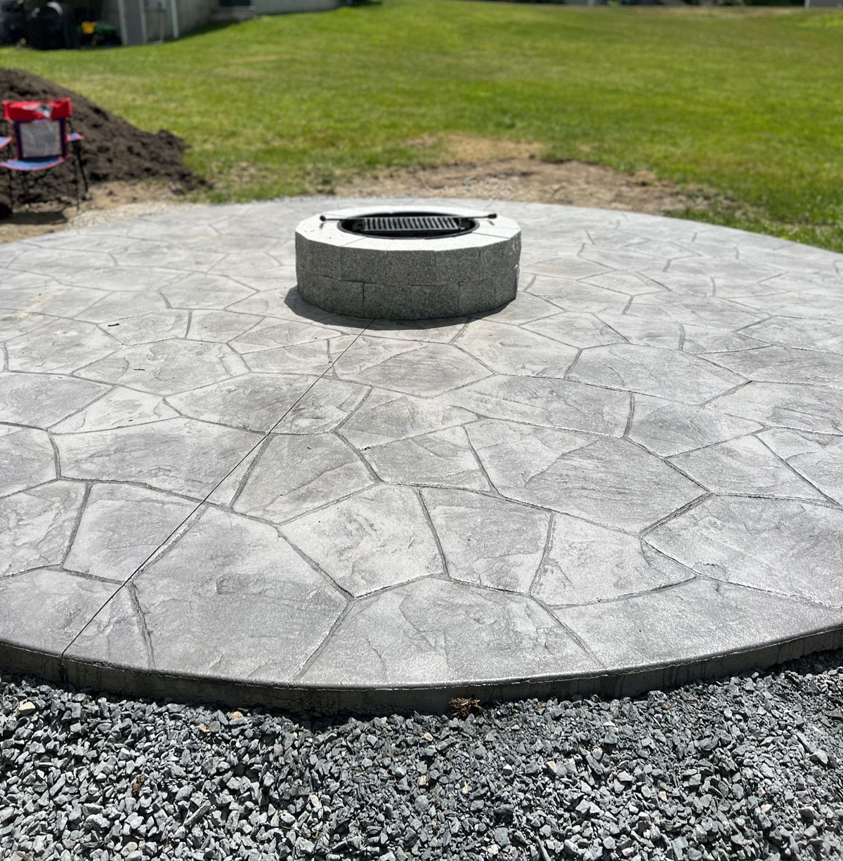 Stamped concrete patio with a circular fire pit in the center, bordered by gravel and grass.