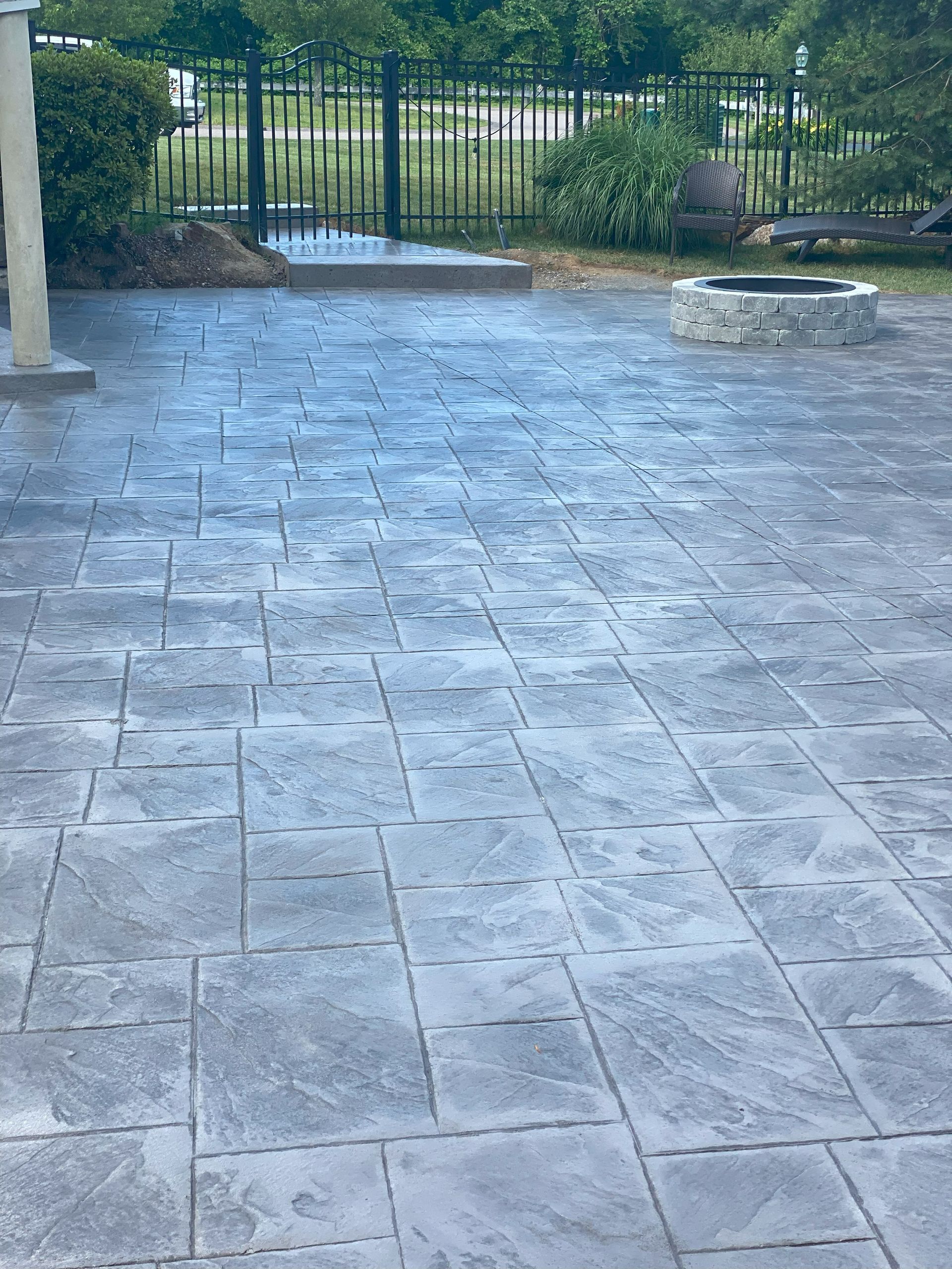 Covered patio with gray stone tile flooring, a metal gate, and a round stone fire pit outdoors.