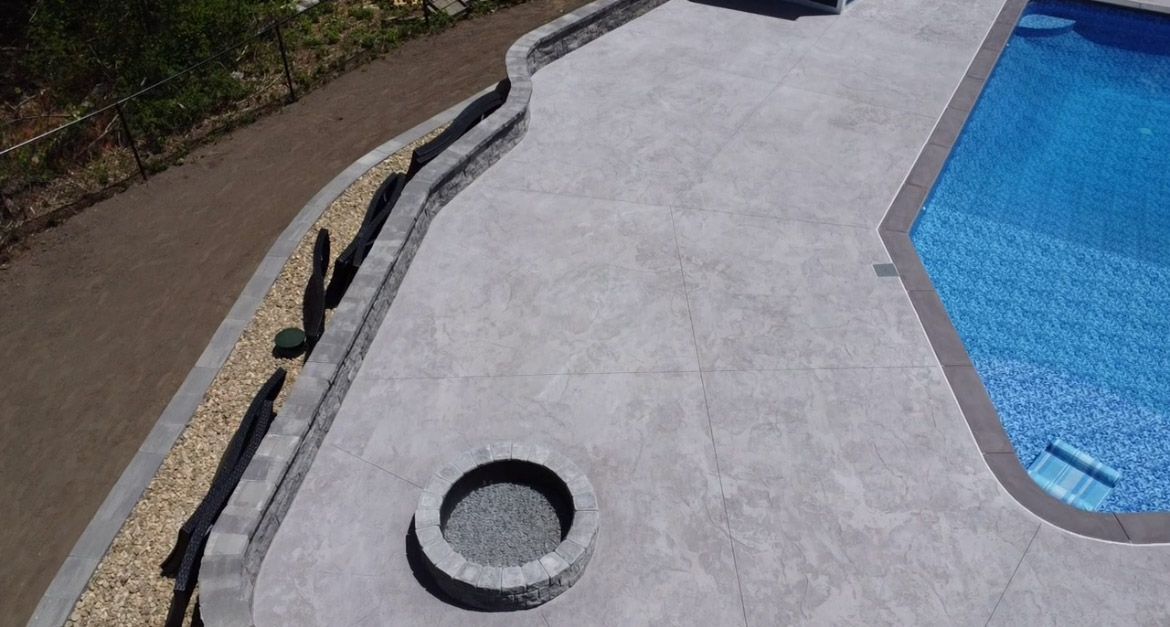 Poolside concrete deck with a drain and black hose beside blue pool water