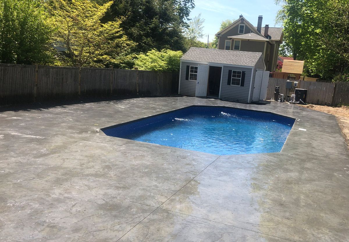 Backyard with a small blue pool, concrete patio, wooden fence, and shed in the background