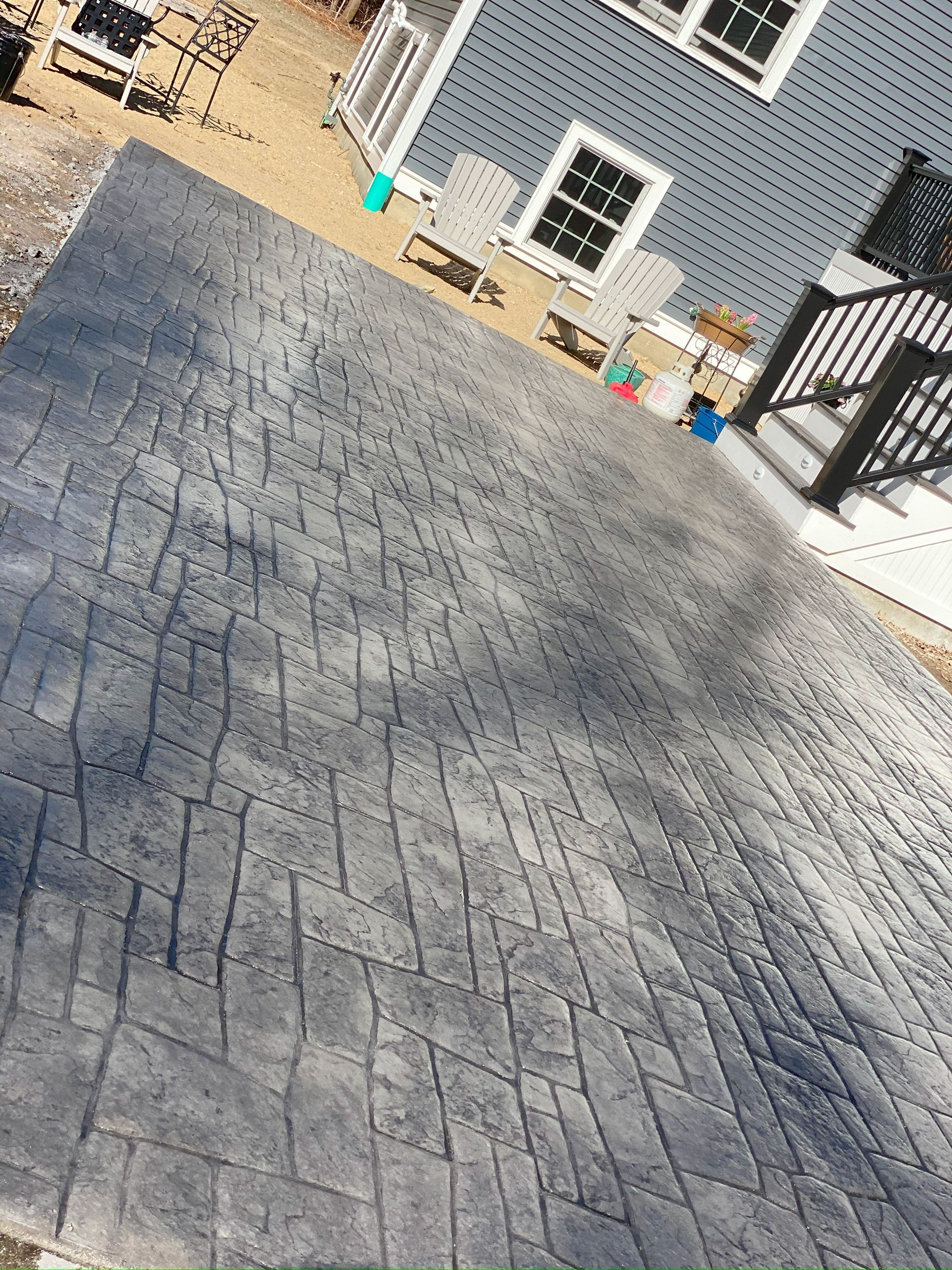 Stamped concrete driveway beside a blue house with windows and patio steps.