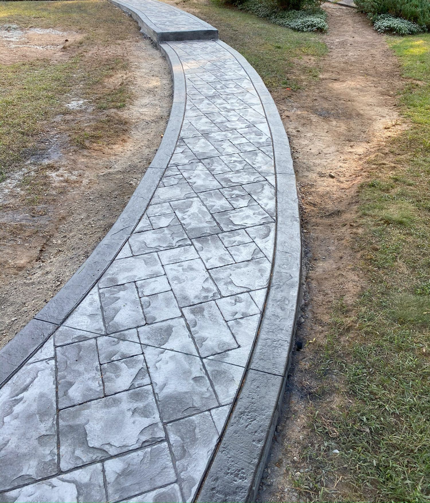 Curved gray stone walkway with concrete borders running through a grassy park area