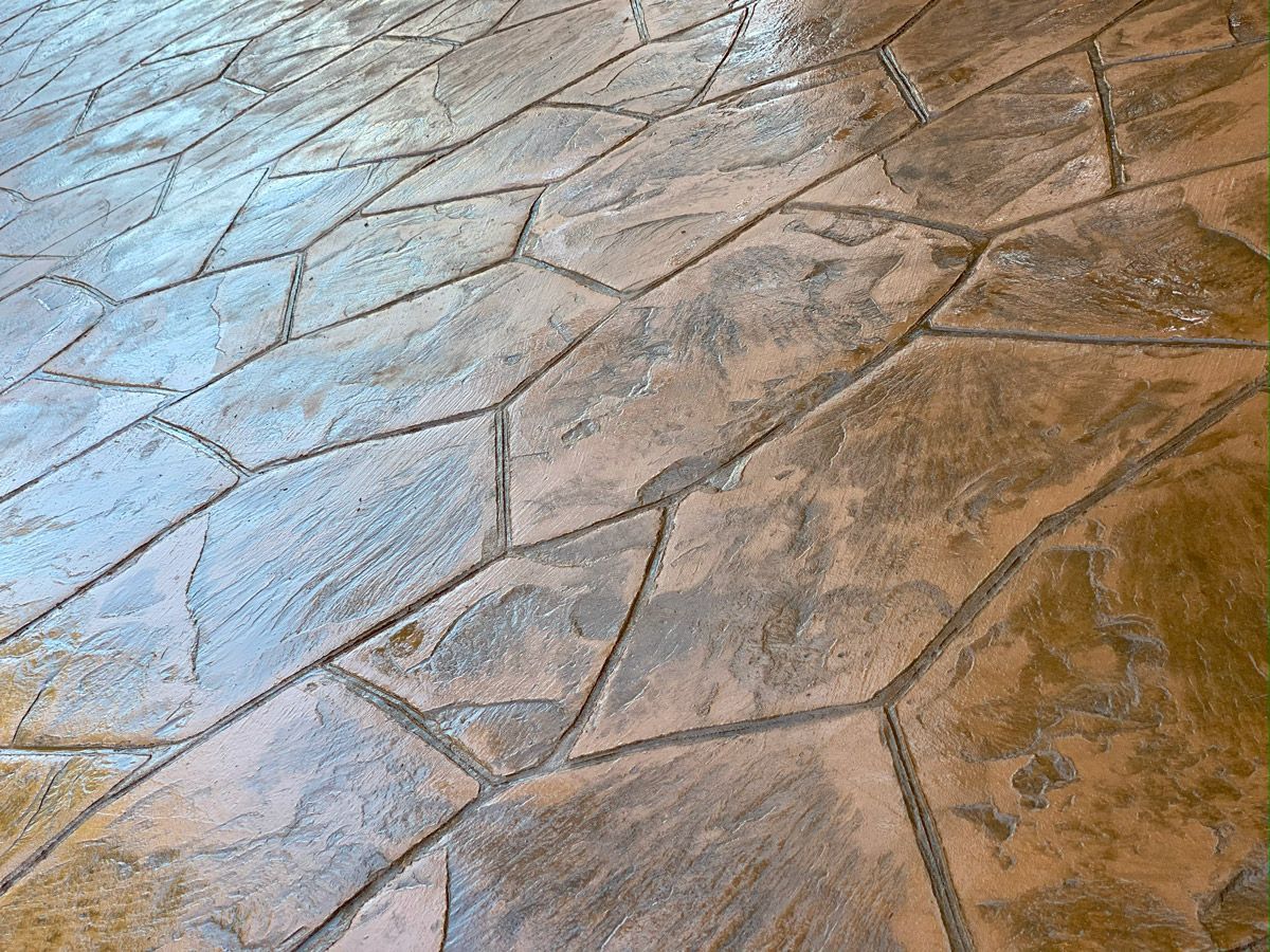 Close-up of textured stamped concrete flooring in tan and gray tones.
