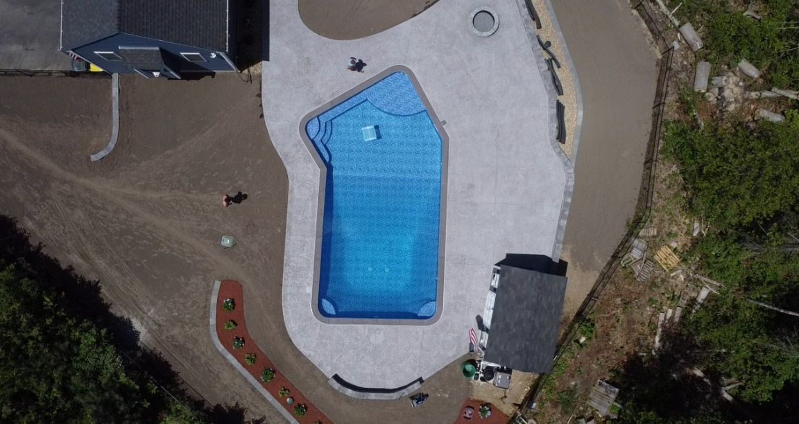 Aerial view of a backyard with a blue swimming pool, patio, and surrounding landscaping