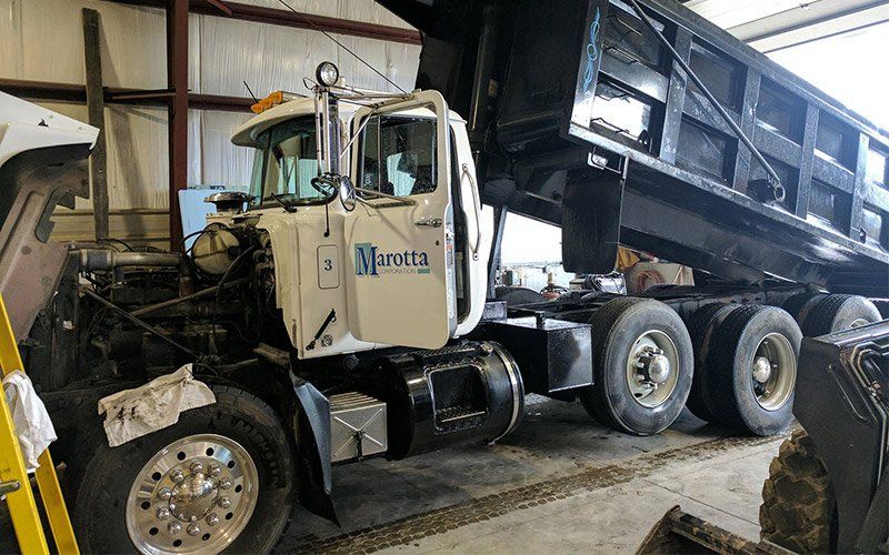 White dump truck inside a warehouse, with raised black bed and damaged front wheel area