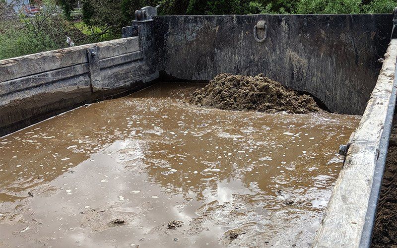Concrete pit filled with muddy water and a pile of dirt against stained walls
