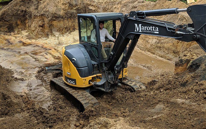 Excavator digging mud in a construction pit, with rocky dirt walls and wet ground.