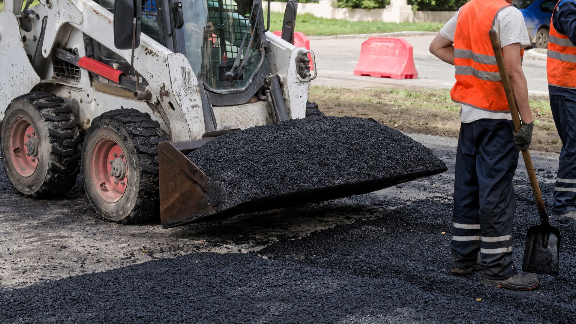 Construction workers spreading black asphalt with a skid-steer loader on a road site
