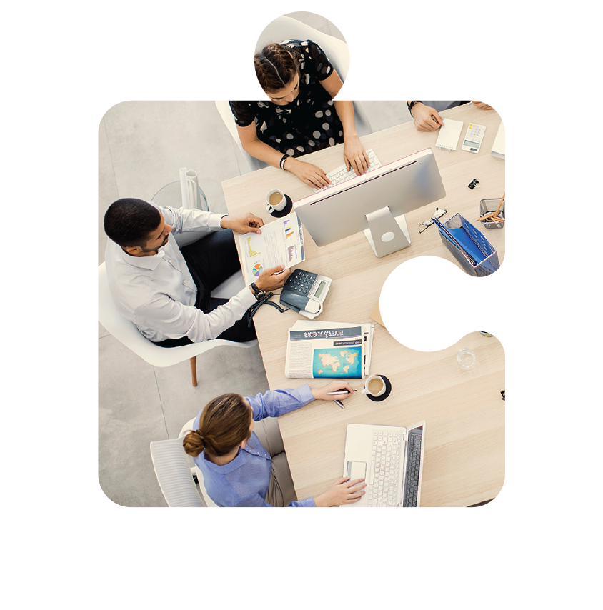 Overhead view of three people collaborating at a desk with laptops, tablets, and office supplies