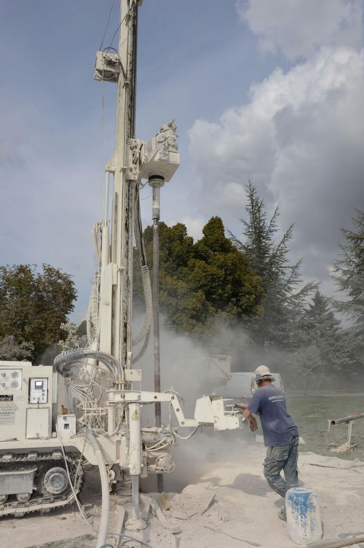 Worker drilling with a tall rig at a dusty construction site