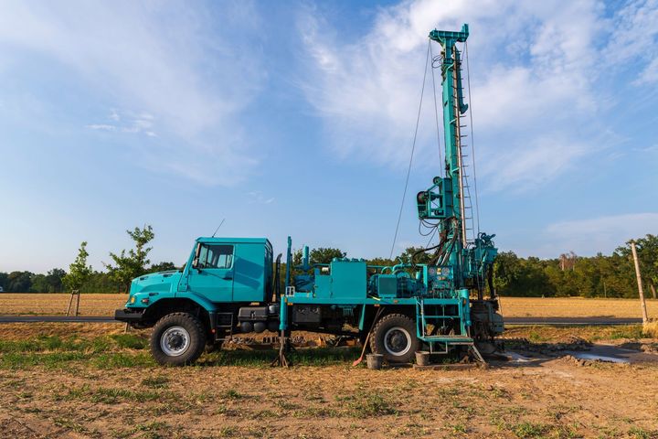 Turquoise drilling truck in a rural field under a blue sky