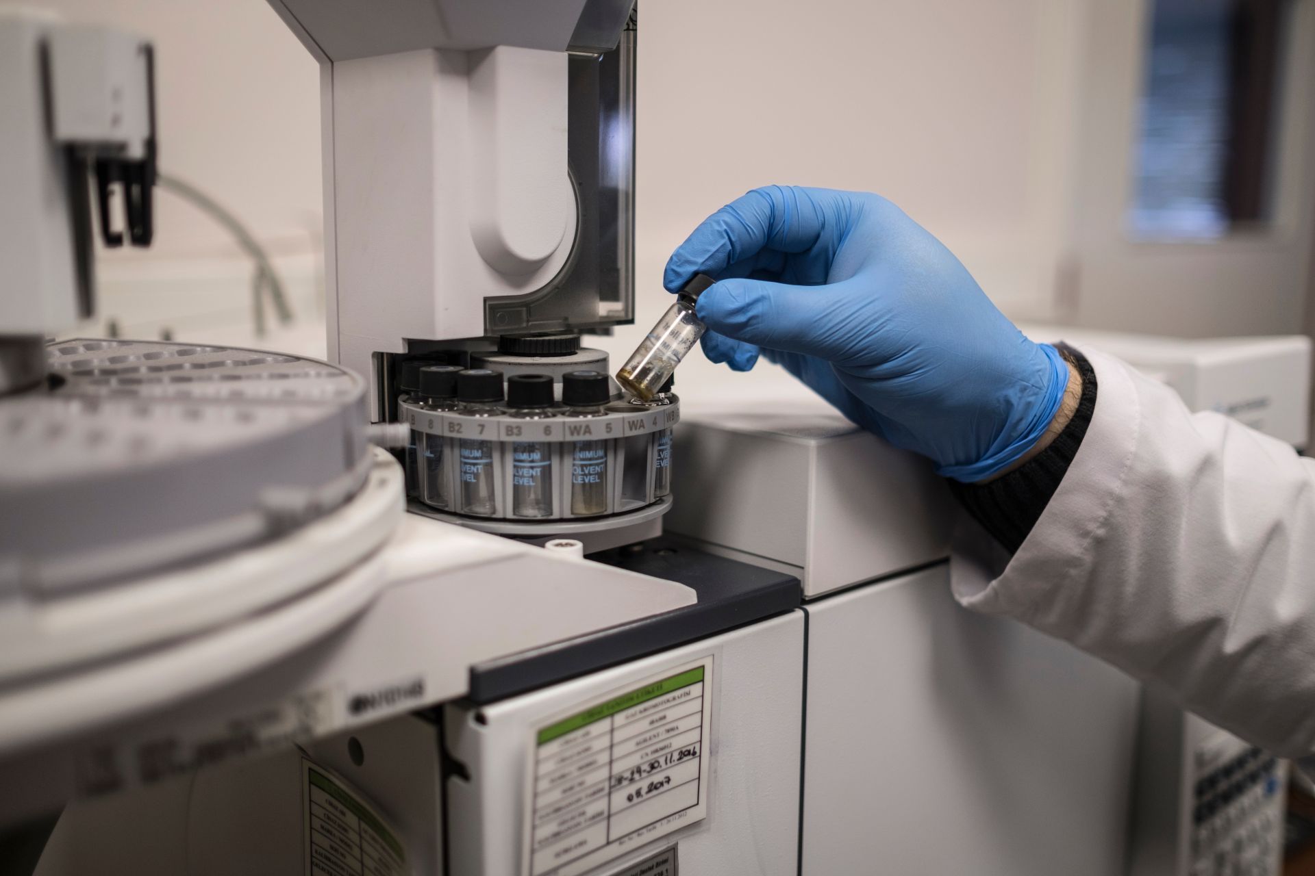 Gloved hand handling a vial in a laboratory instrument