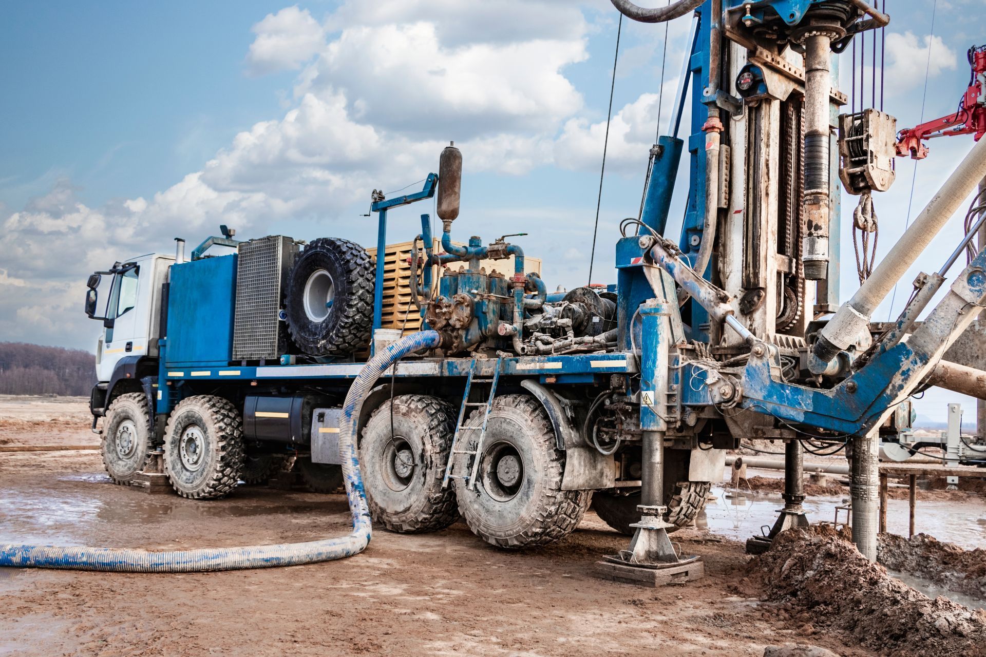 Blue drilling truck at a muddy construction site, boring into the ground with hoses and equipment attached