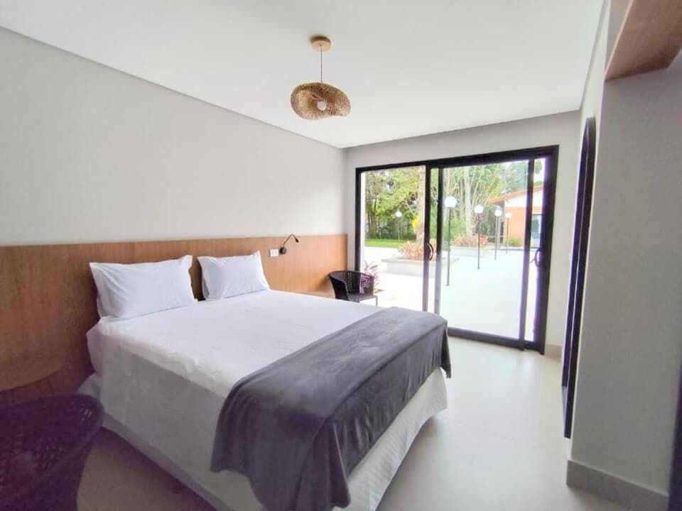Quarto de hotel moderno com cama grande, cabeceira de madeira e portas de vidro deslizantes para um pátio.