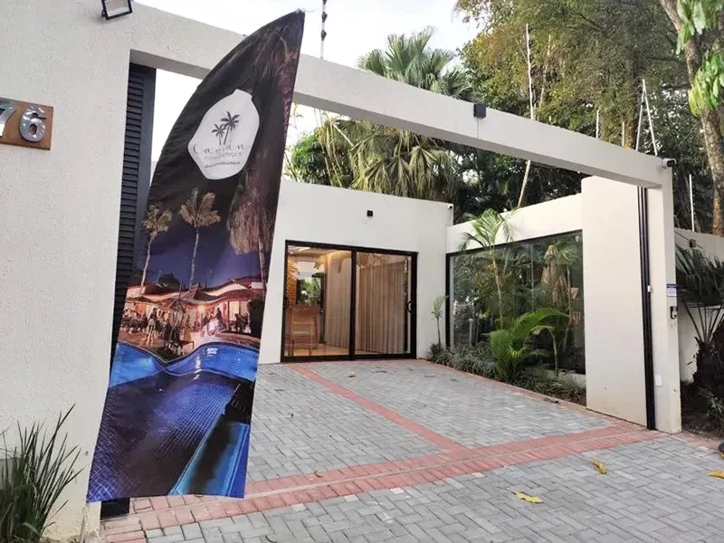 Entrada moderna de uma casa branca com garagem, portas de vidro e uma grande placa junto ao portão.