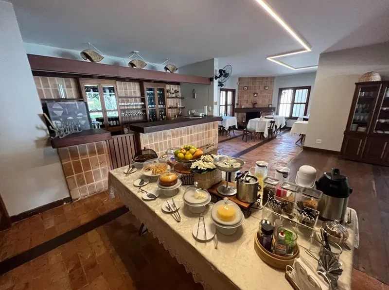 Mesa de buffet em uma cozinha moderna com café, chá, frutas e doces sob luzes brilhantes.