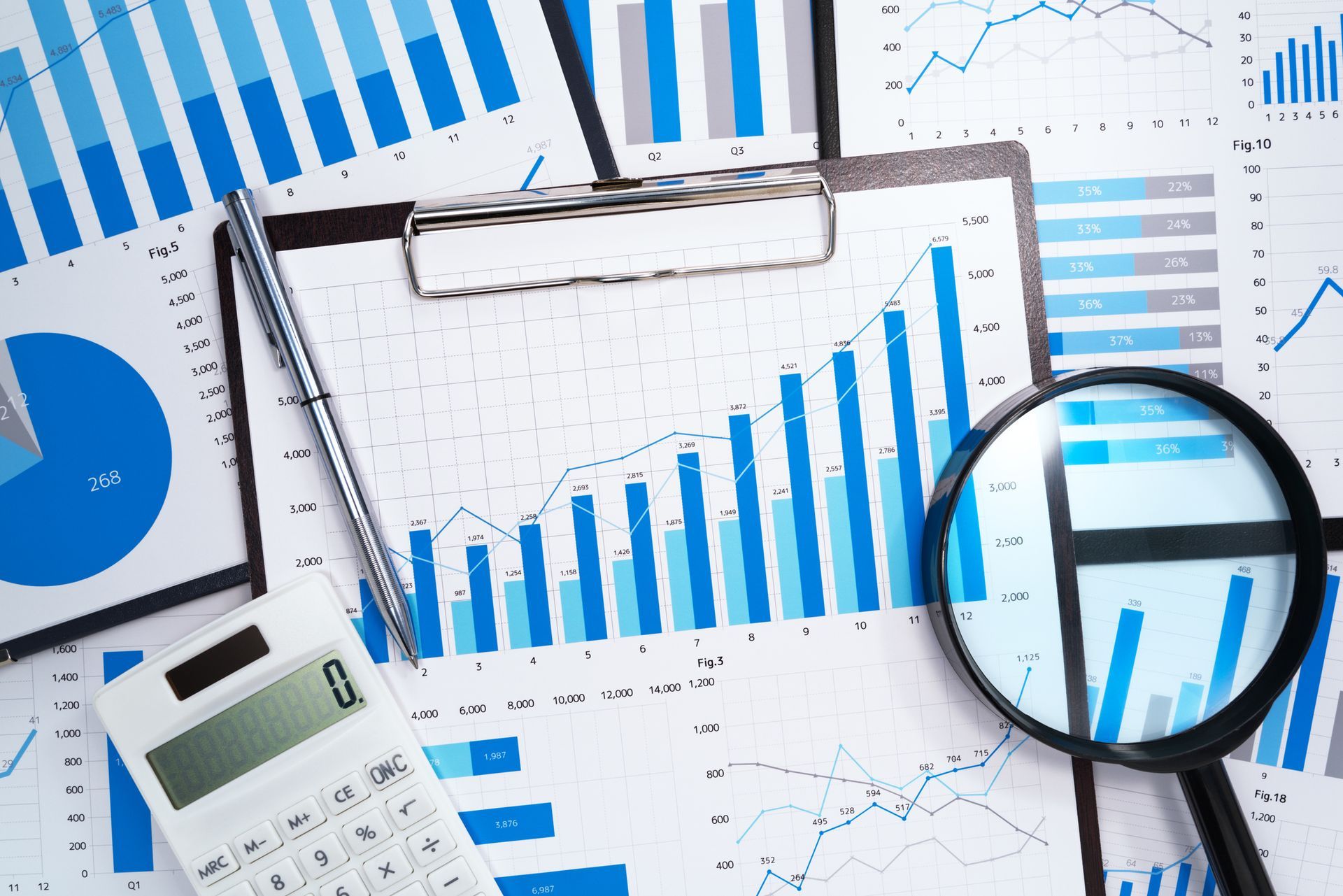 Blue graphs, charts, and financial data with calculator, magnifying glass, and pen.