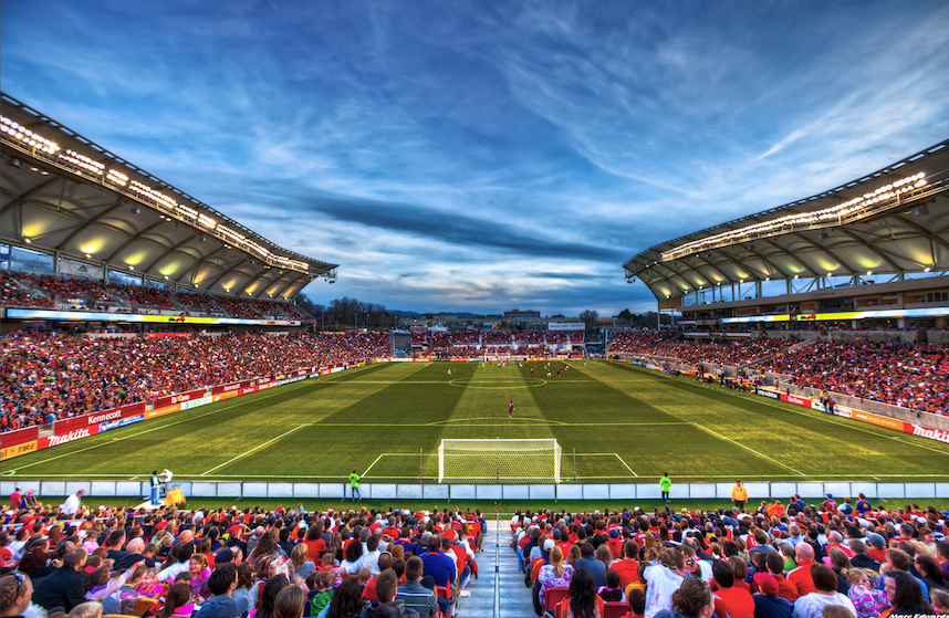 Stadium AV soltuions. Soccer stadium packed with fans, green field, under a cloudy blue sky.