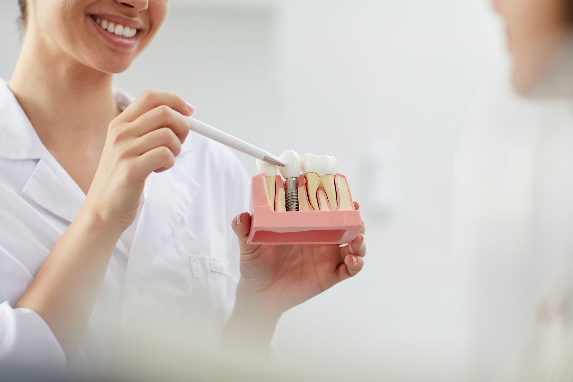 Dentist smiling, pointing to a teeth model with a probe, explaining dental health to a patient.