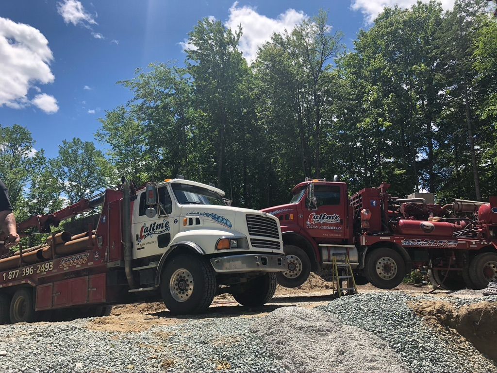 Deux camions de chantier sont stationnés près d'une zone boisée. L'un est blanc, avec le logo « AJ Leising », et l'autre est rouge.