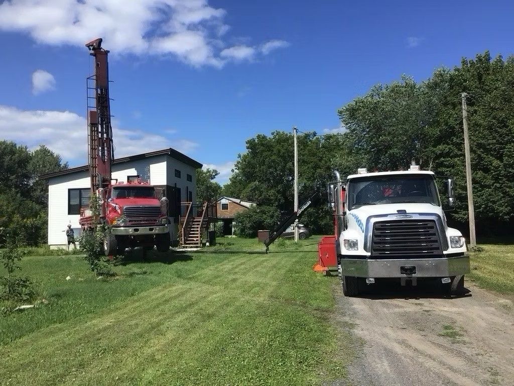 Deux camions de forage devant un bâtiment blanc, sur un terrain herbeux sous un ciel d'un bleu éclatant.