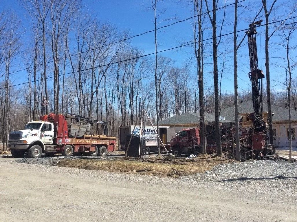 Camion et matériel de forage près d'un bâtiment en construction dans une zone boisée par une journée ensoleillée.