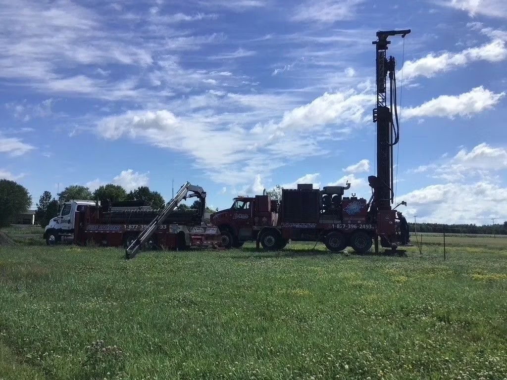 Plateforme de forage sur un champ verdoyant sous un ciel bleu parsemé de nuages épars.