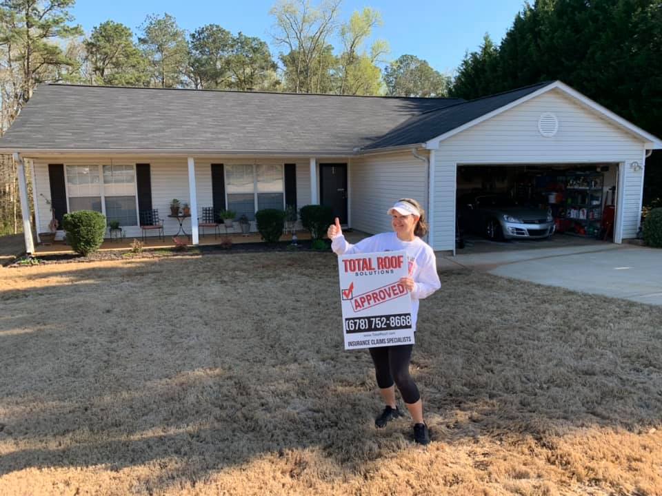 woman standing in front of Total Roof Solutions repaired home