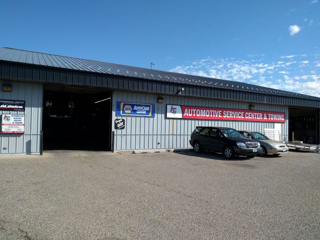 Auto repair shop exterior with open garage door and two parked cars under a blue sky | I29 Automotive Repair