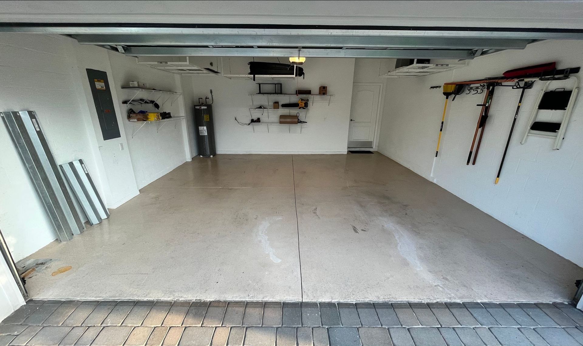 Empty, clean garage with light-colored epoxy floor and white walls. Tools and shelves are mounted on the walls.