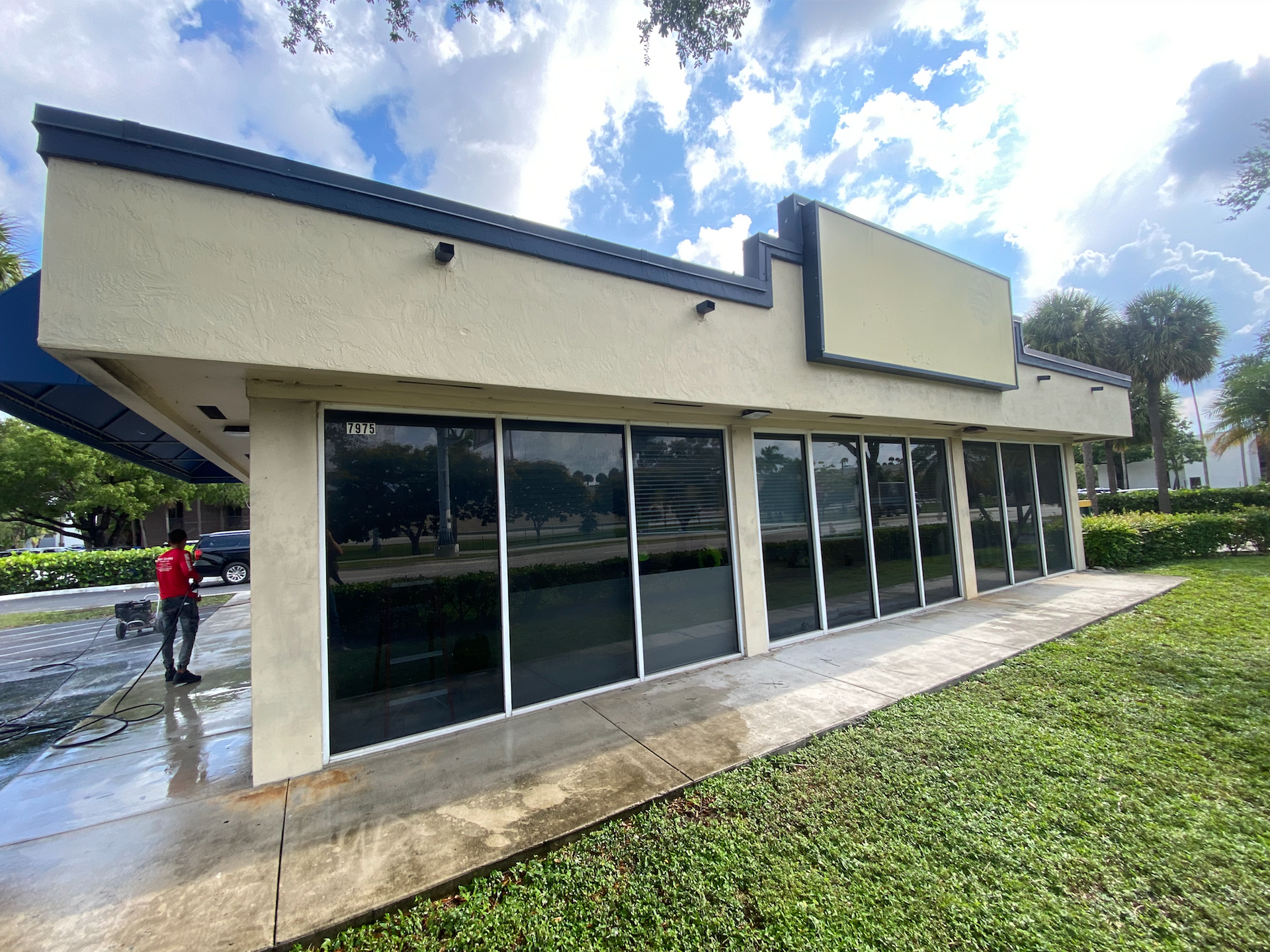 Exterior view of a commercial building with dark tinted windows, blue trim, and a person in red.