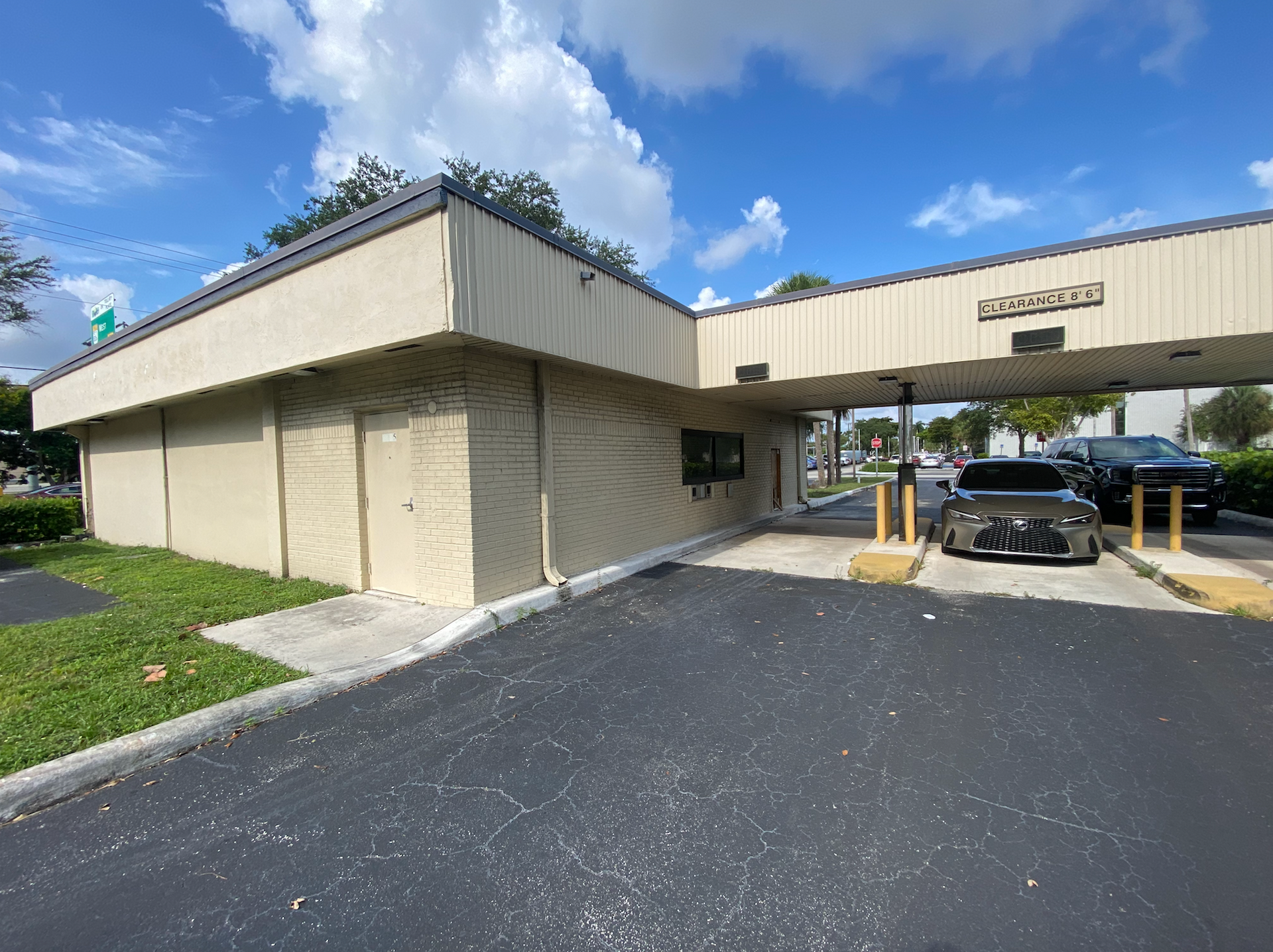 Exterior view of a drive-thru bank. A gray car is at the window. Building is beige with a dark asphalt driveway.
