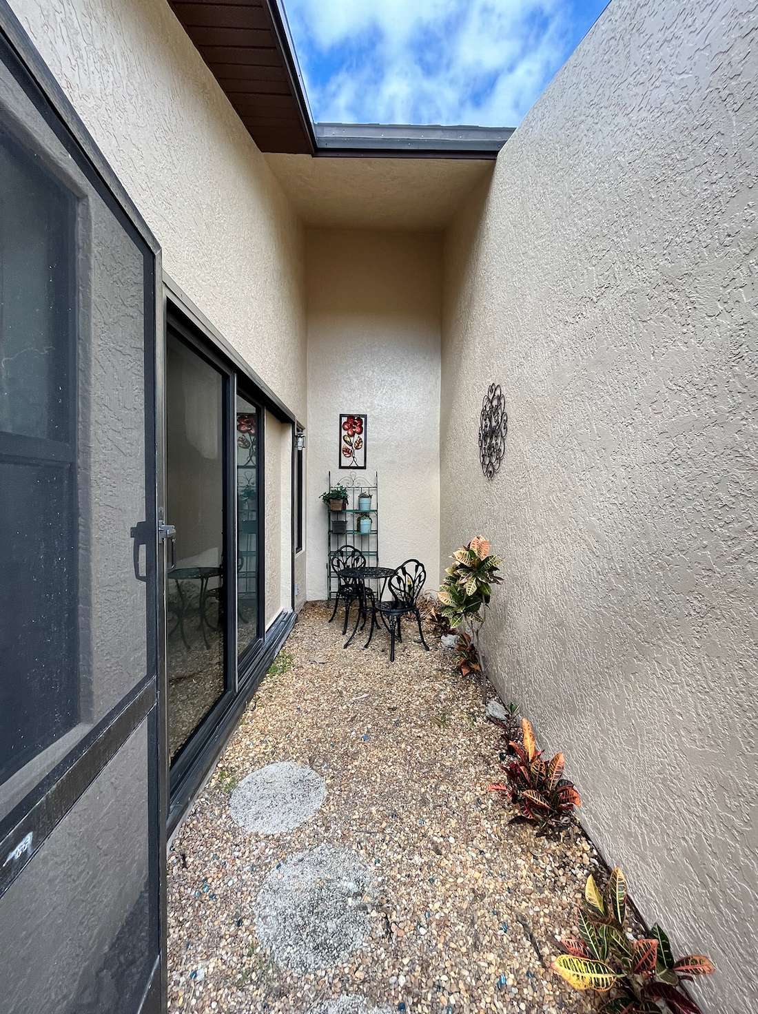 Narrow outdoor patio with stone ground, small table and chairs, and high textured walls.