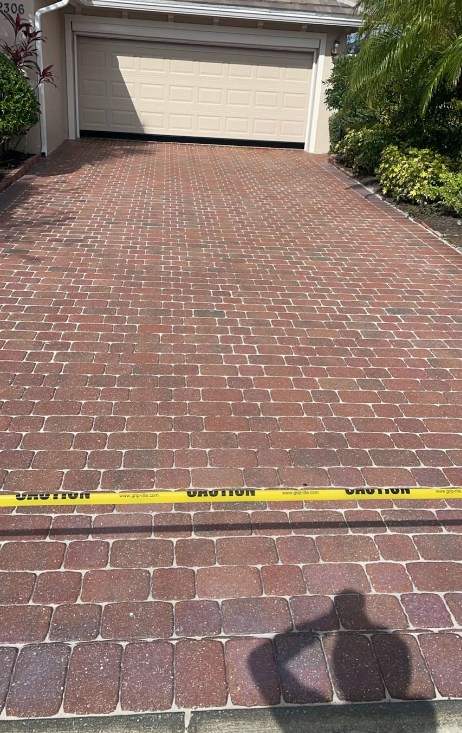 Red brick driveway leads to a garage. Yellow caution tape is across the driveway.