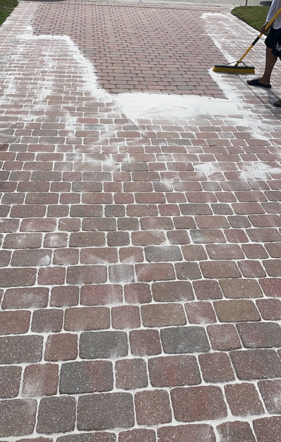 Person brushing white substance onto brick pavers outdoors.