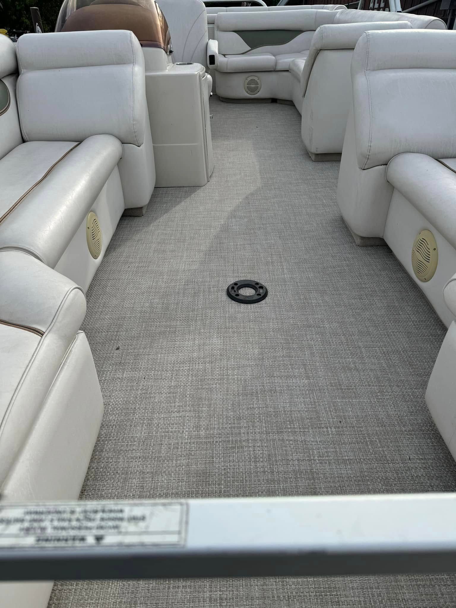 Empty white upholstered boat seating around a gray carpeted deck aisle