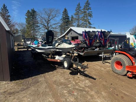 Boat on trailer in a snowy yard with trees and a red tractor nearby.