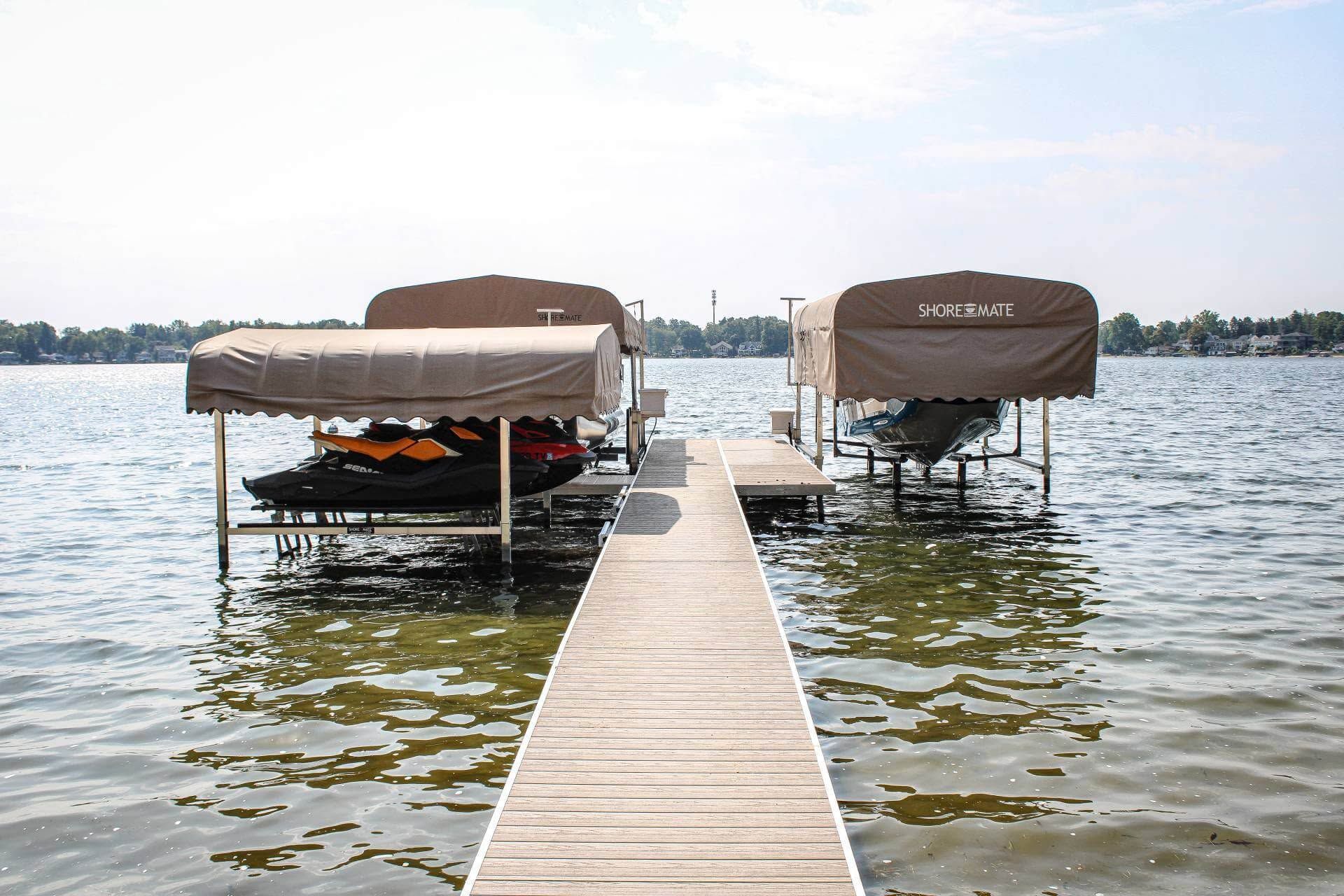 Dock leading to two covered boats on a calm lake under a bright sky