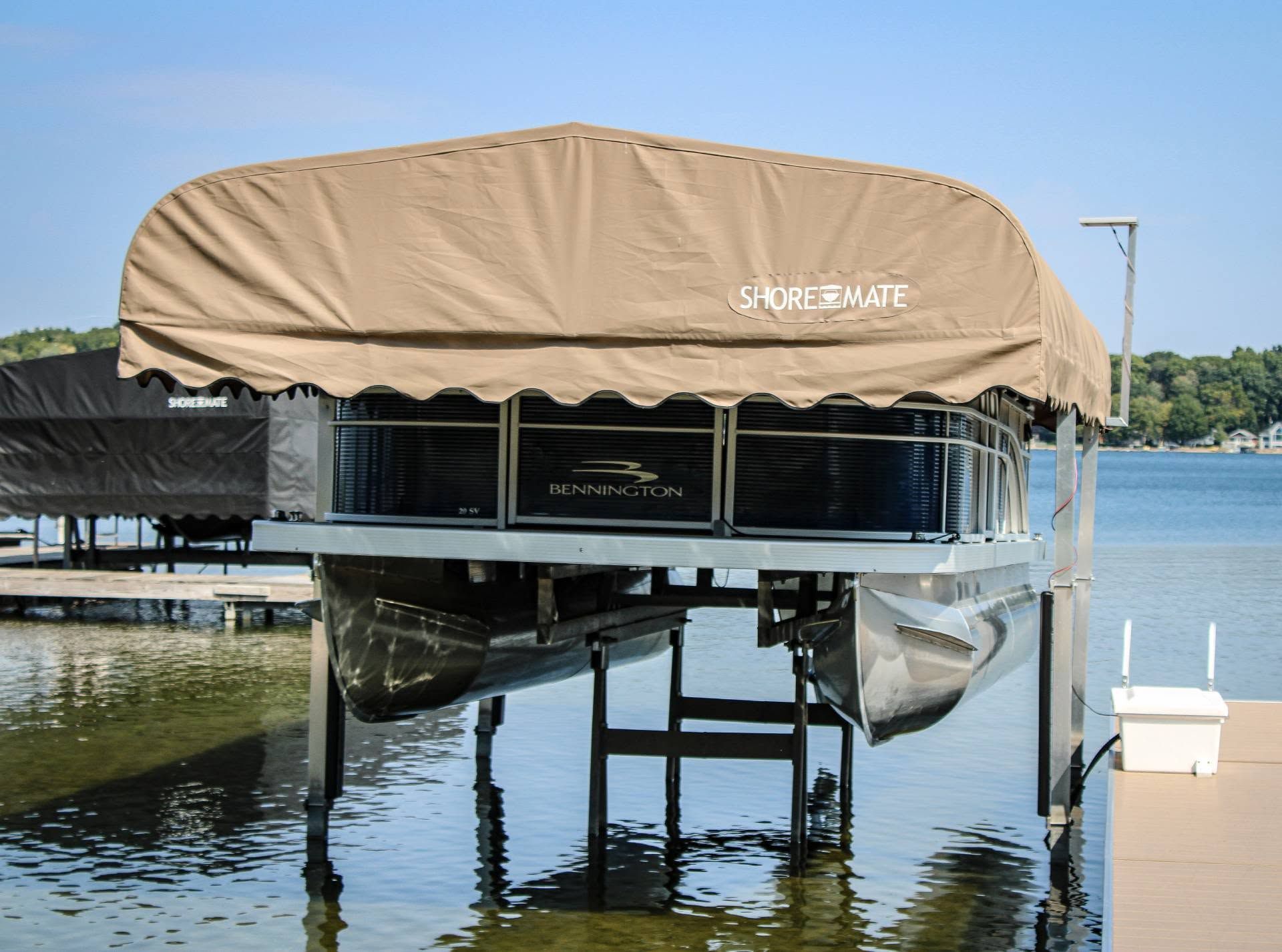 Covered boat lift over a dock on calm water beside a sandy shoreline