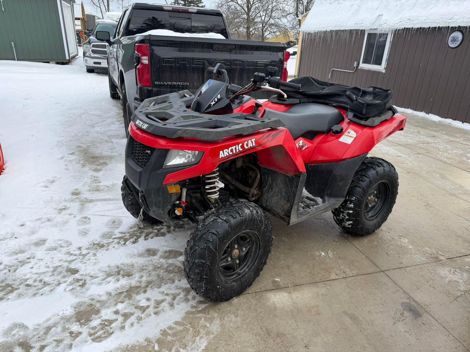 Red ATV parked on a snowy driveway beside a black pickup truck.