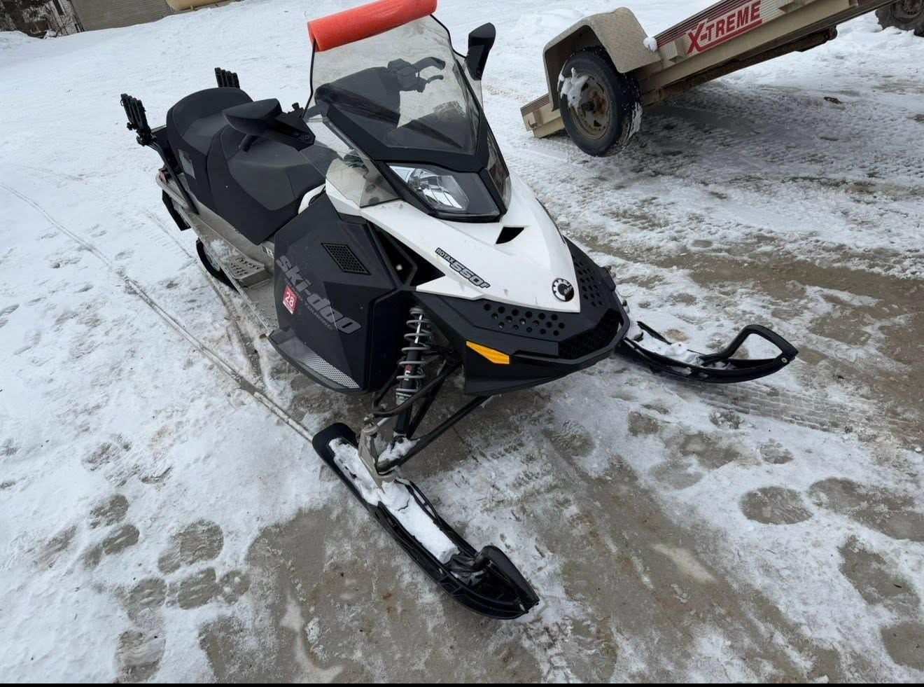 Black and white snowmobile parked on snowy ground near a trailer.