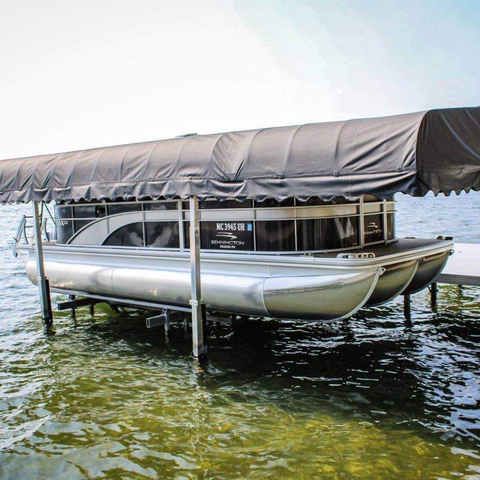 Pontoon boat with gray canopy docked on clear green water under a covered lift