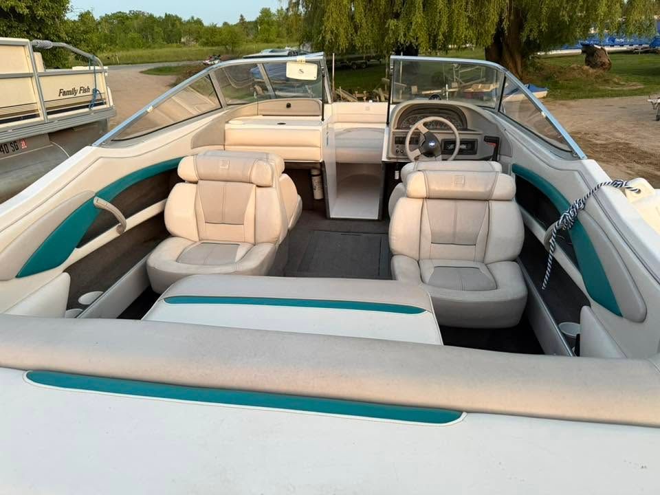 Interior view of a white-and-teal speedboat with cream seats and a steering wheel on calm water.