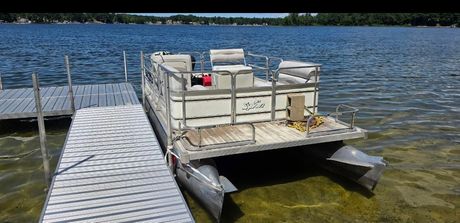 Small docked boat with beige crates beside a floating pier on a calm lake