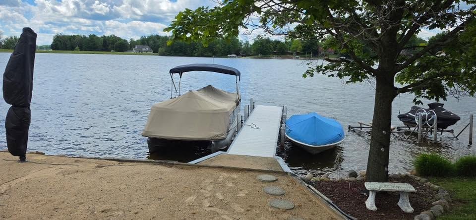 Two covered boats docked by a lakeside shore under a tree